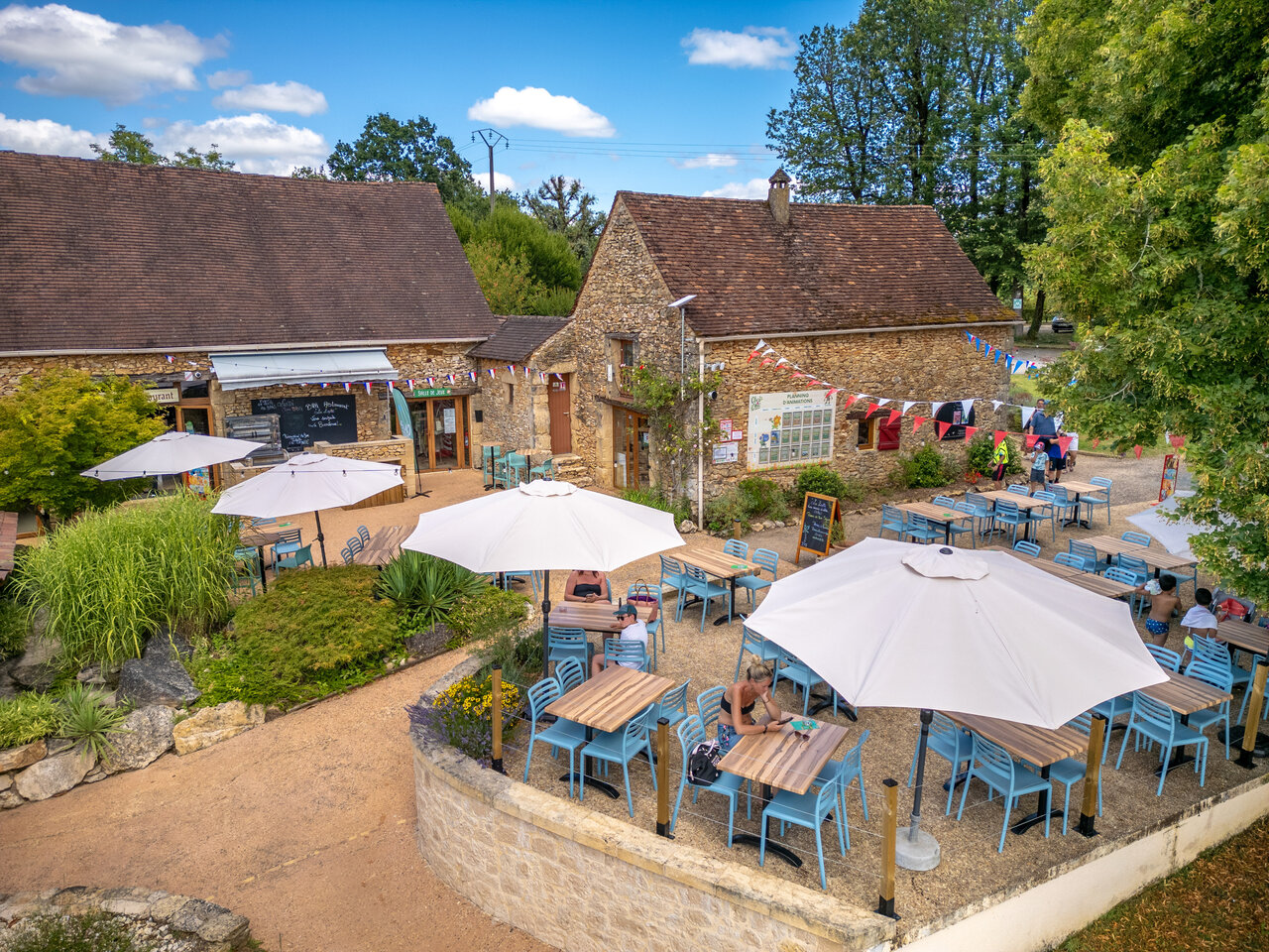 Outdoor terrace of restaurant and bar with parasols at CLICOCHIC Linotte campsite, Le Bugue.
