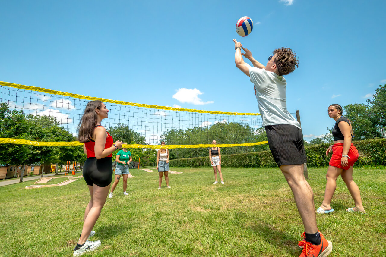 Lively volleyball game on sports court at CLICOCHIC Linotte campsite in Le Bugue.