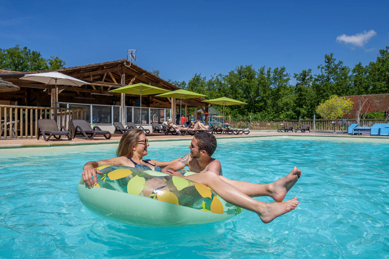 Outdoor pool, smiling couple on inflatable ring. Camping CLICOCHIC Lou Castel.