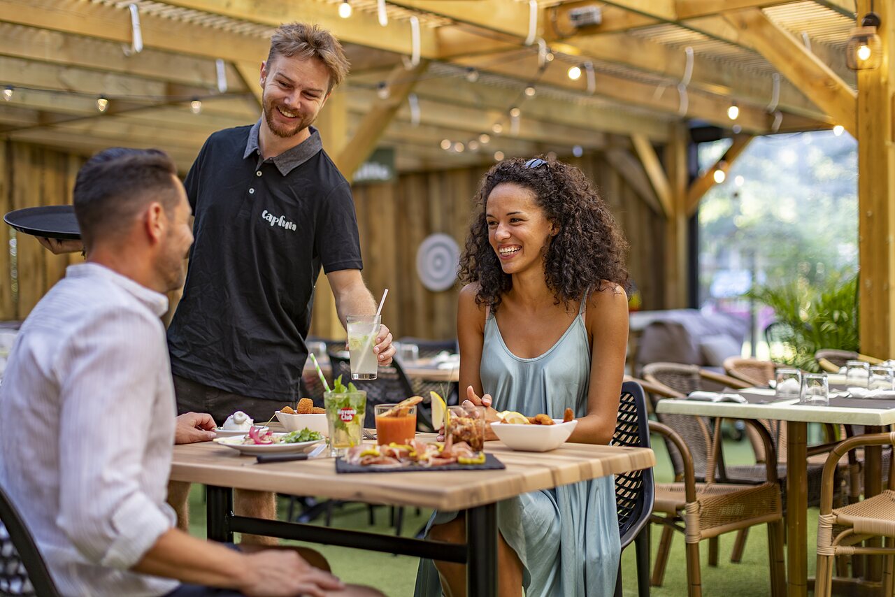 Couple dining on terrace, smiling waiter at CAPFUN Lou Puntaou in LEON.