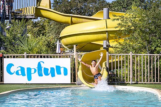 Gelbe Wasserrutsche und Kind im Pool auf dem Campingplatz CAPFUN Lou Puntaou in LEON.