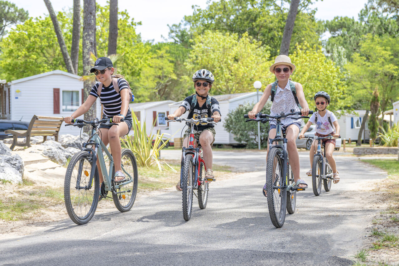 Smiling children cycling on a path, Mobile homes in background at VAGUES OCEANES Marina Landes campsite in Mimizan (40).