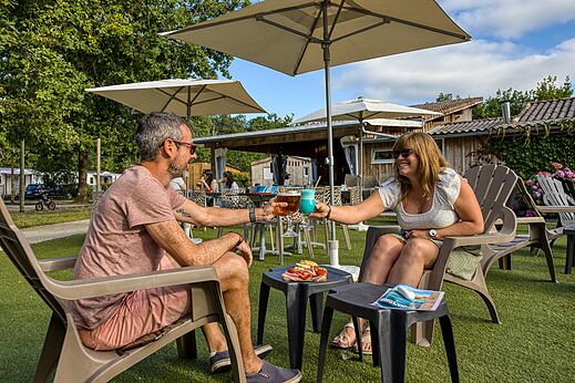 Paar stößt mit Cocktails an der Bar des Campingplatzes CLICOCHIC Médoc Bleu in Carcans (33) an.