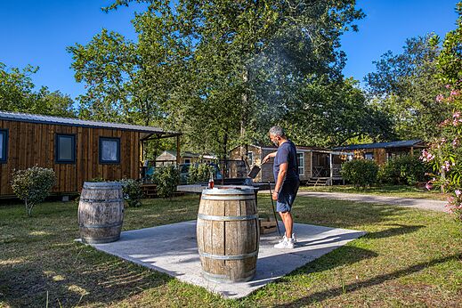 Mann grillt vor Mobilheimen im Camping CLICOCHIC Médoc Bleu in Carcans (33).
