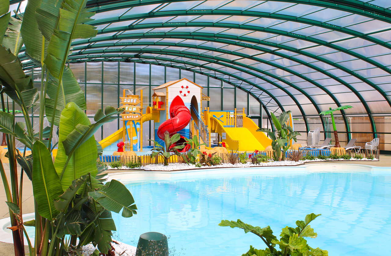 Indoor swimming pool, red slide and water games at CAPFUN Mer campsite.