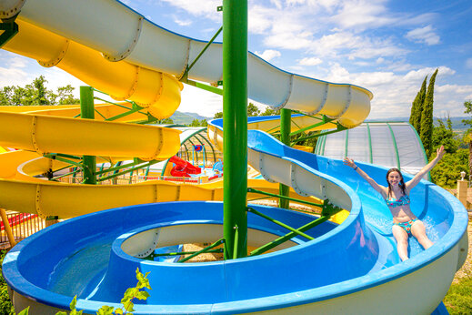 Junge Frau rutscht blaue Wasserrutsche hinunter auf Camping CAPFUN Merle Roux in Baix (07).