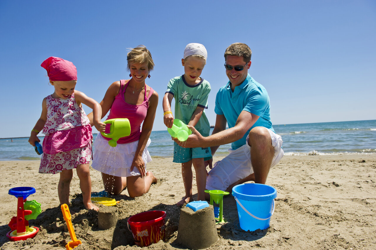 Familie baut Sandburgen am Strand auf dem Campingplatz CAPFUN Mer et Soleil in Cap d'Agde.