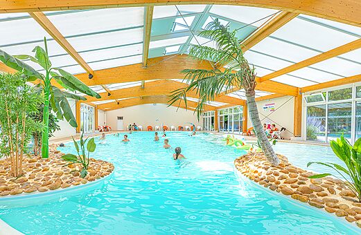 Tropisches Hallenbad mit Palmen und Badegästen auf dem Campingplatz VAGUES OCEANES Michelière, Givrand (85).