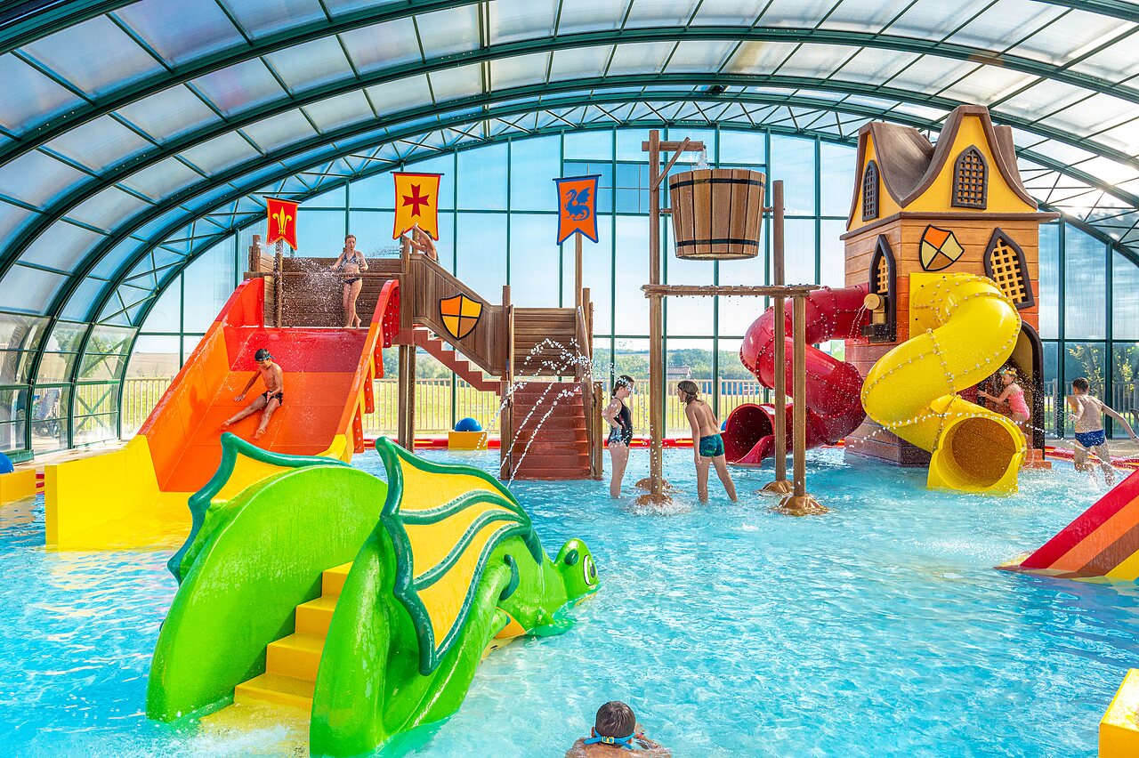 �berdachtes Schwimmbad mit Rutschen, Wasserspielen und Kindern auf dem Campingplatz CAPFUN Mirabelle in VOLSTROFF (57).