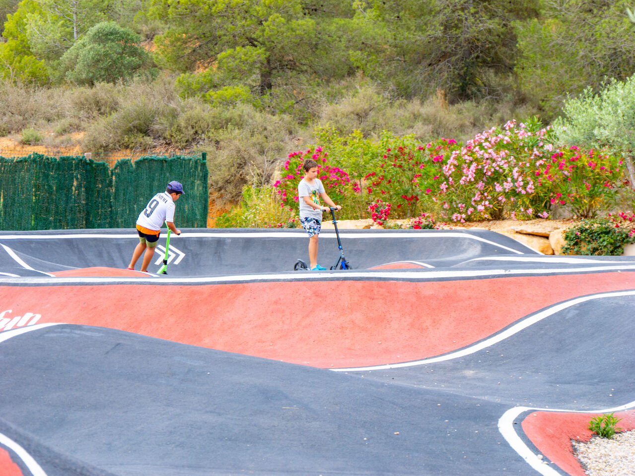 Pump-Track-Anlage mit Kindern auf Rollern auf dem Campingplatz CAPFUN Montblanc Park in Montblanc (43).