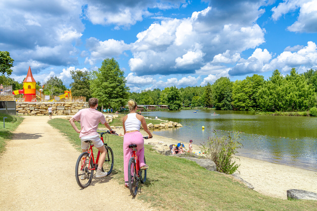 Couple cycling on path near lake and playground at CAPFUN Moulinal campsite in BIRON (24).