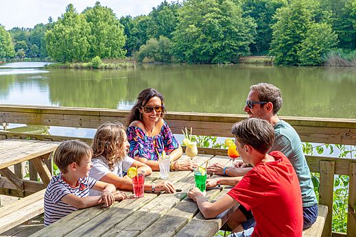 Famille souriante buvant des cocktails sur une terrasse au bord du lac au camping CAPFUN Moulinal à BIRON (24).