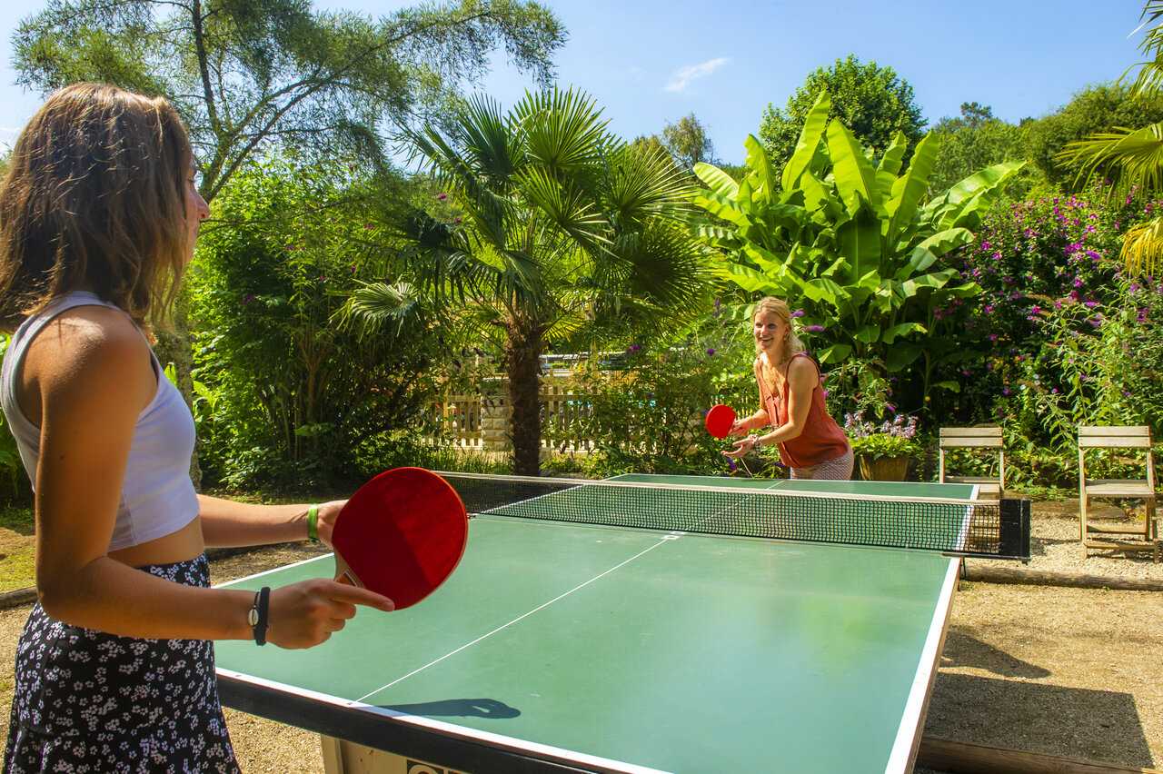 Two women playing outdoor table tennis at camping CLICOCHIC Moulin du Roch.