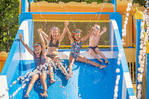 Lachende Kinder auf Wasserrutsche auf dem Campingplatz CLICOCHIC Moulin du Roch in Saint Andre D'Allas.