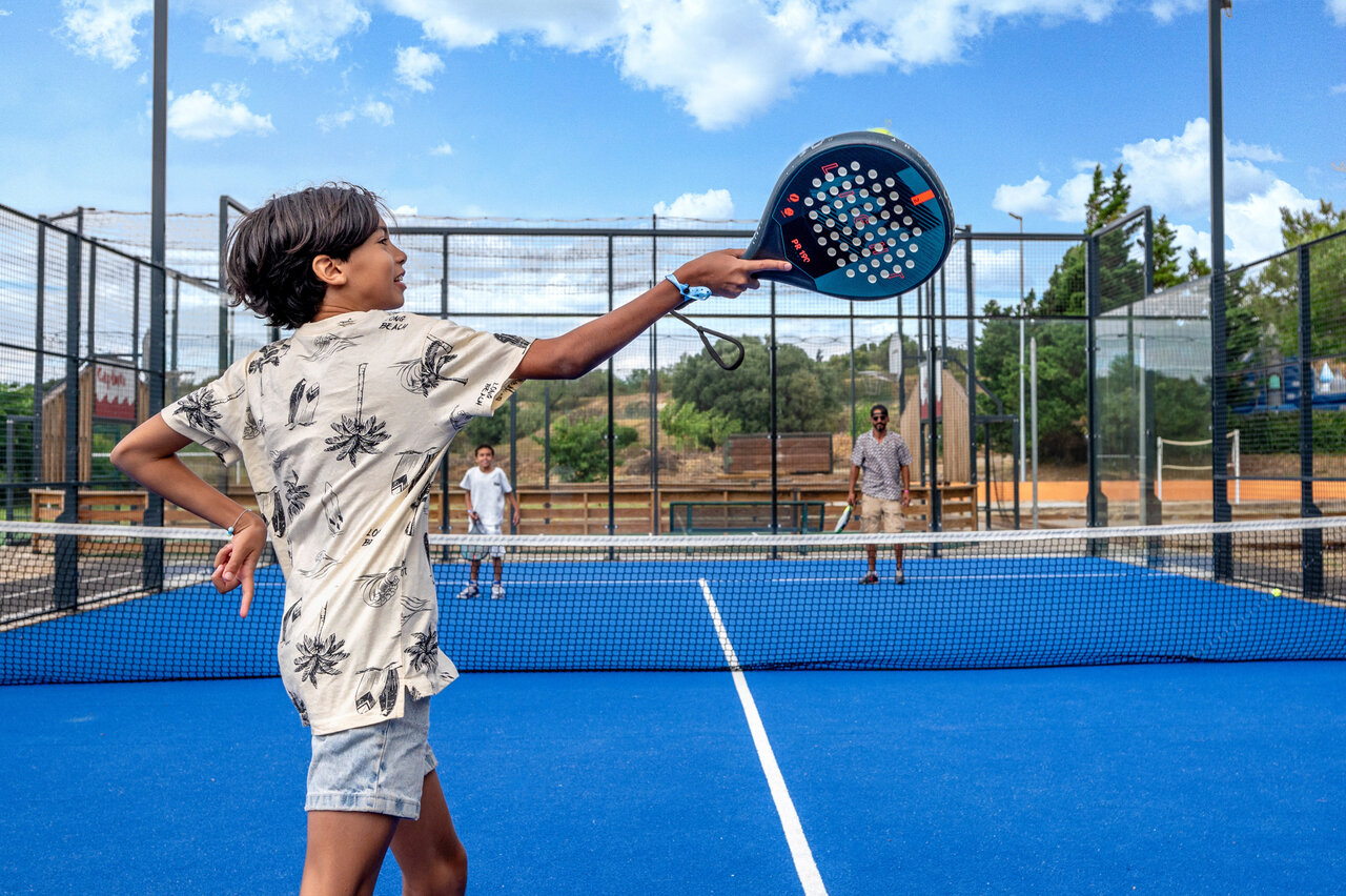 Blue padel court with child playing, at CAPFUN La Nautique campsite in Narbonne (11).