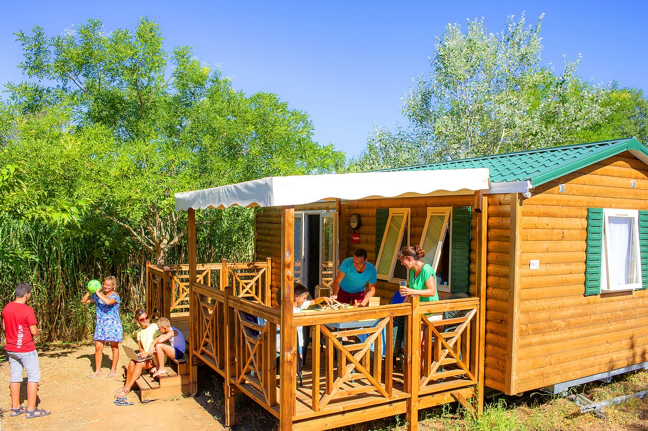 Familie genie�t Holz-Mobilheim-Terrasse auf Campingplatz CAPFUN La Nina in Agde (34).