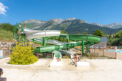 Wasserrutschen und spielende Kinder, mit Bergen im Hintergrund auf dem Campingplatz CAPFUN Oursière in Villard de Lans (38).