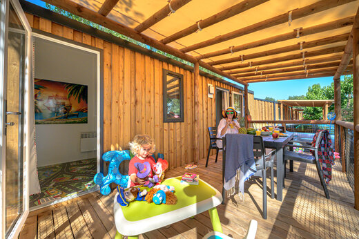 Möblierte Terrasse eines Mobilheims mit spielendem Kind und Erwachsenem auf Camping CAPFUN Pachacaid in La Mole (83).