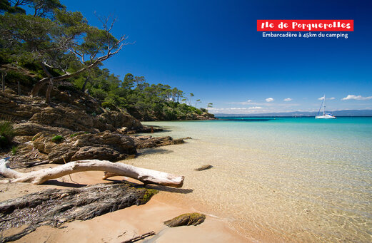 Paradijselijk strand van Île de Porquerolles, turquoise water, rotsachtige kust en zeilboot.