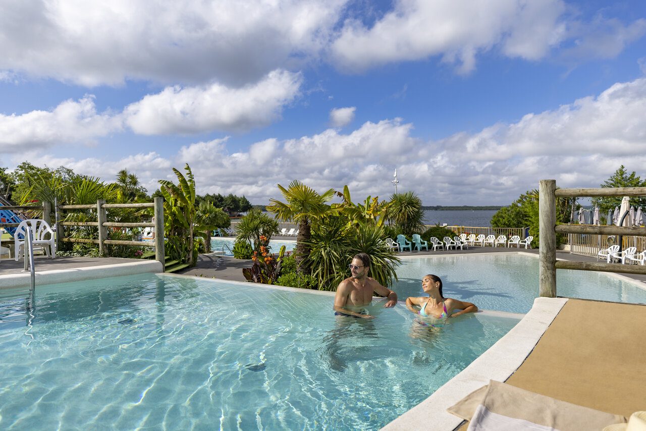 Outdoor swimming pool with couple, lush vegetation, at CAPFUN Paillotte campsite in AZUR (40).