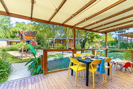 �berdachte Terrasse mit Esstisch und Spielplatz auf dem Campingplatz CAPFUN Paradis de Bazas in BAZAS (33).