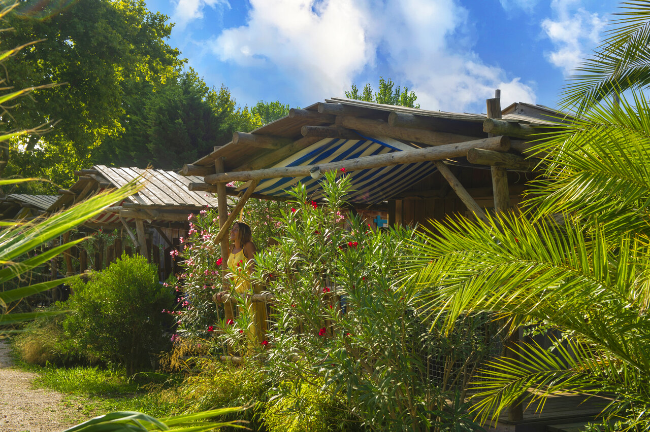 Wooden accommodation with flowery terrace and lush vegetation at CAPFUN Paris Roussillon campsite.
