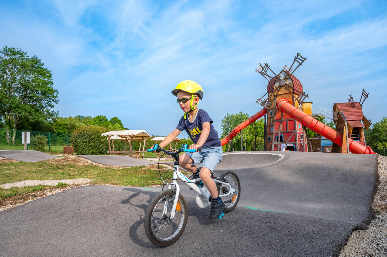 Child on bike on pump track with windmill playground at CAPFUN Pergola campsite in Marigny (39).