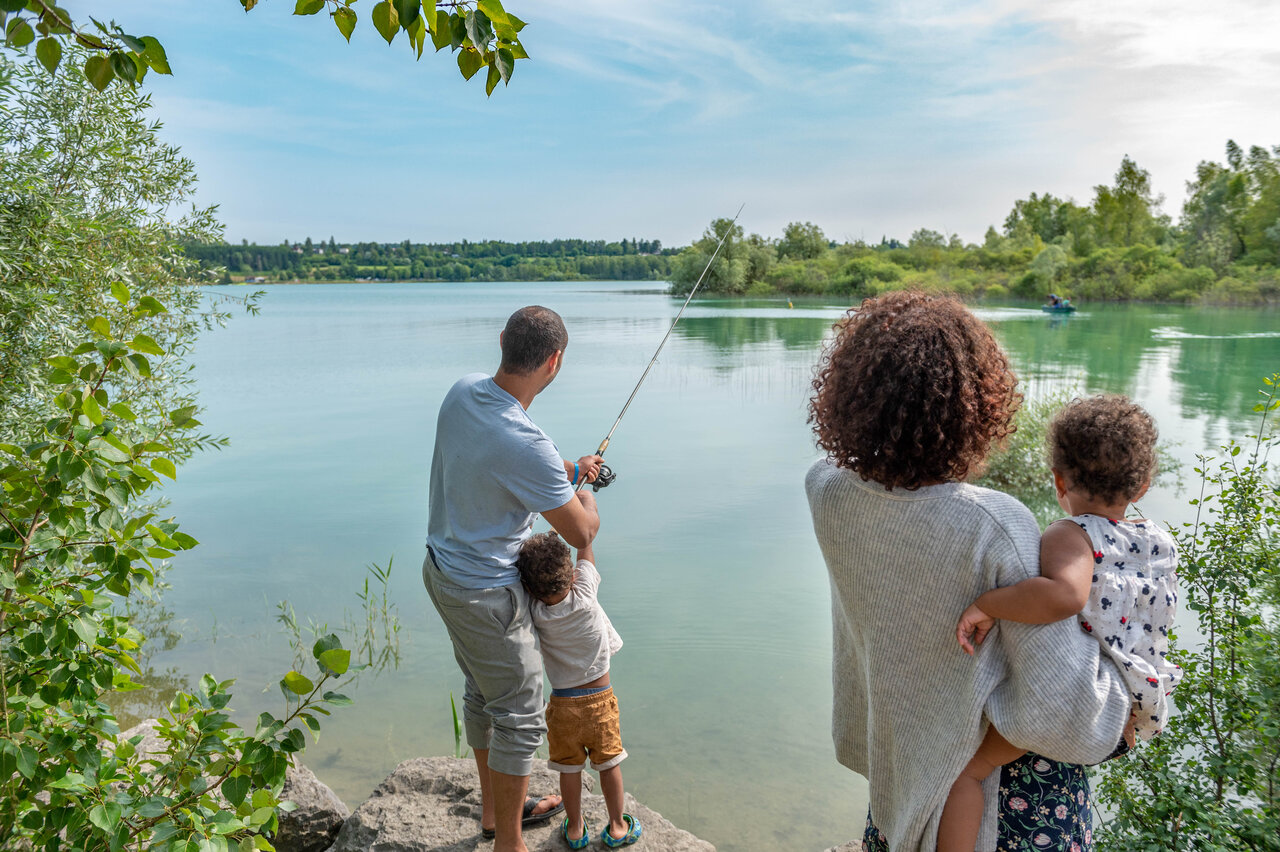 Family fishing by peaceful lake shore, lush nature at CAPFUN Pergola campsite in Marigny (39).