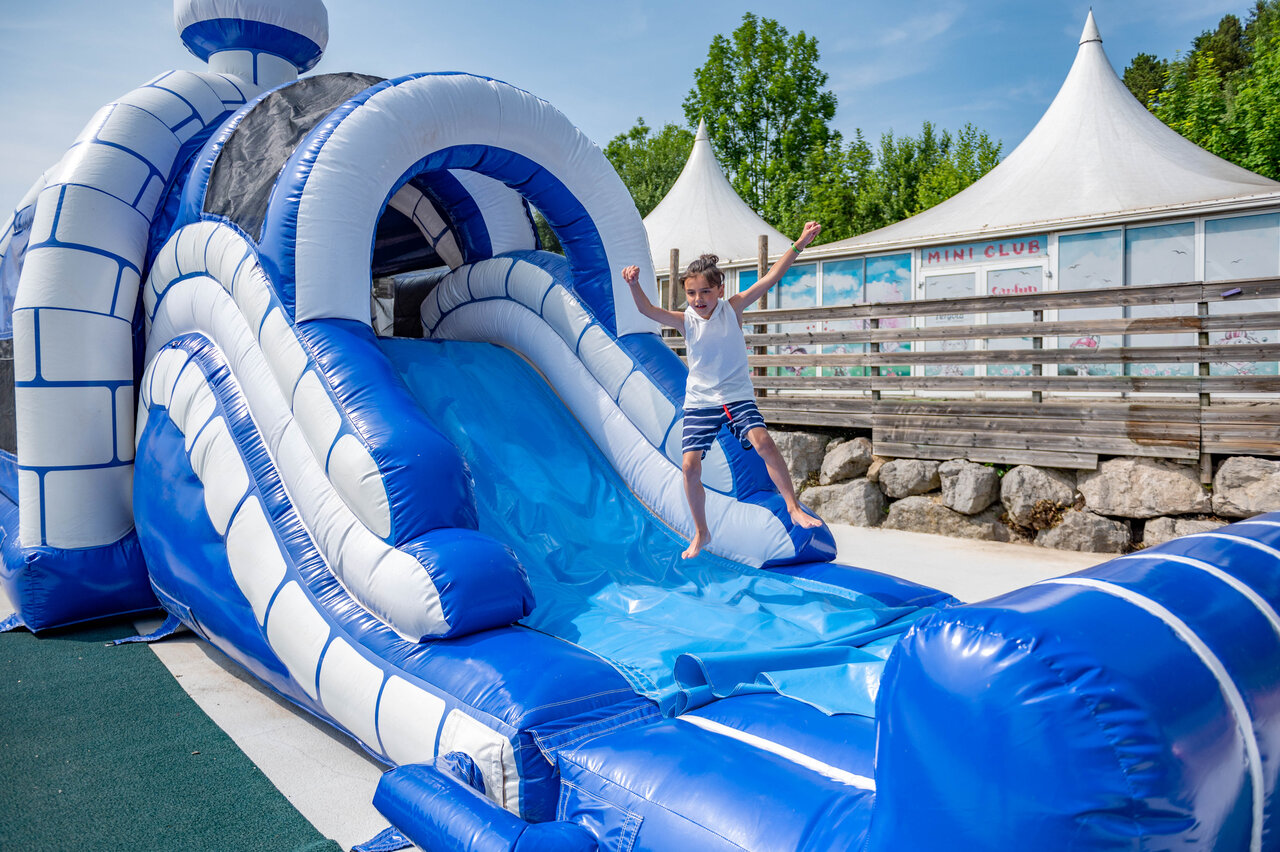 Blue and white inflatable slide, child jumping, at CAPFUN Pergola campsite in Marigny (39).