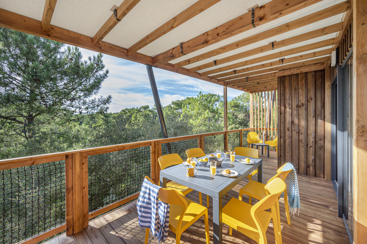 Holzterrasse eines Mobilheims mit Tisch und gelben St�hlen, Waldblick auf dem Campingplatz CLICOCHIC Petit Bec in St Hilaire de Riez (85).