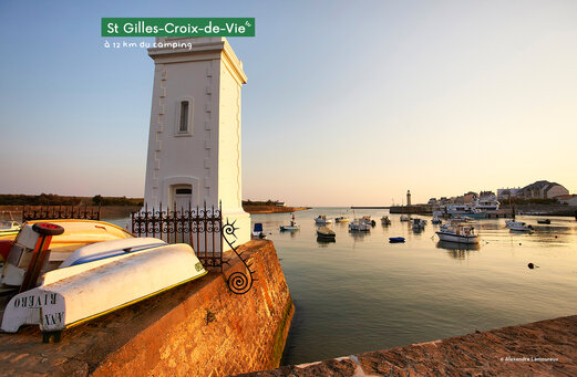 Hafen von Saint-Gilles-Croix-de-Vie mit Booten und Leuchtturm bei Sonnenuntergang.