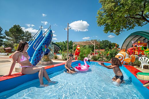 Kinderen en jonge vrouw spelen in speelzwembad met glijbaan op camping CAPFUN Pinèdes du Luberon in PERTUIS (84).