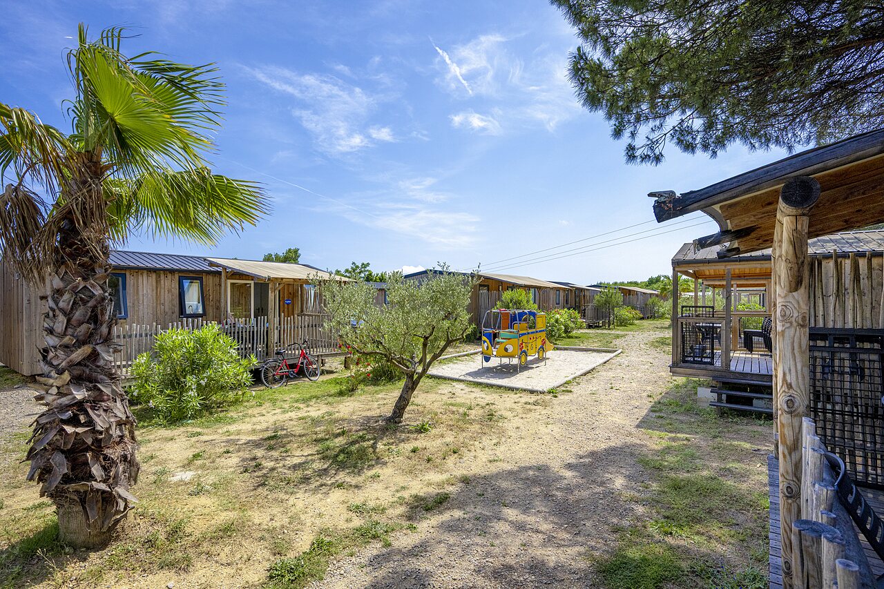 Holz-Mobilheime, Spielplatz und Palmen auf dem Campingplatz CAPFUN La Pin�de de Grimaud in Grimaud (83).