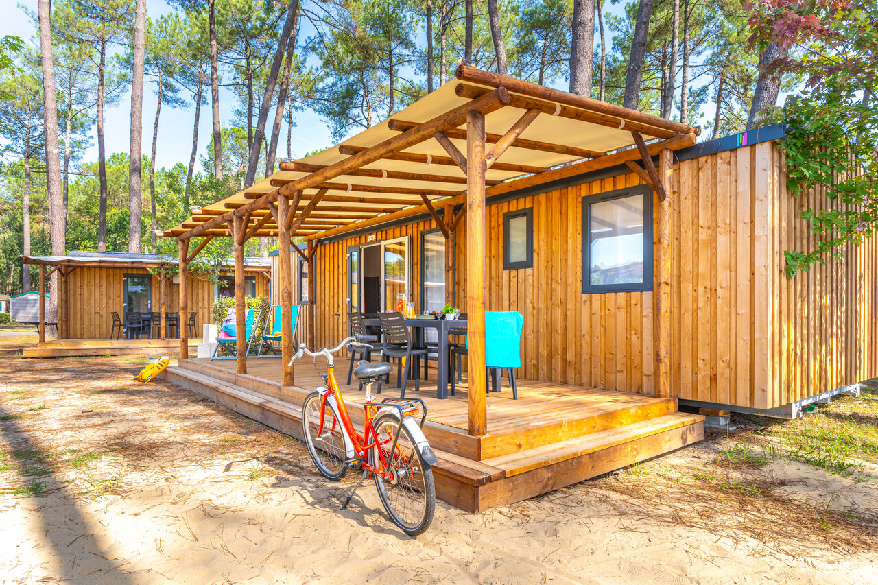 Wooden mobile home with covered terrace and bicycle, at CAPFUN Pomme de Pin campsite in Saubion (40).