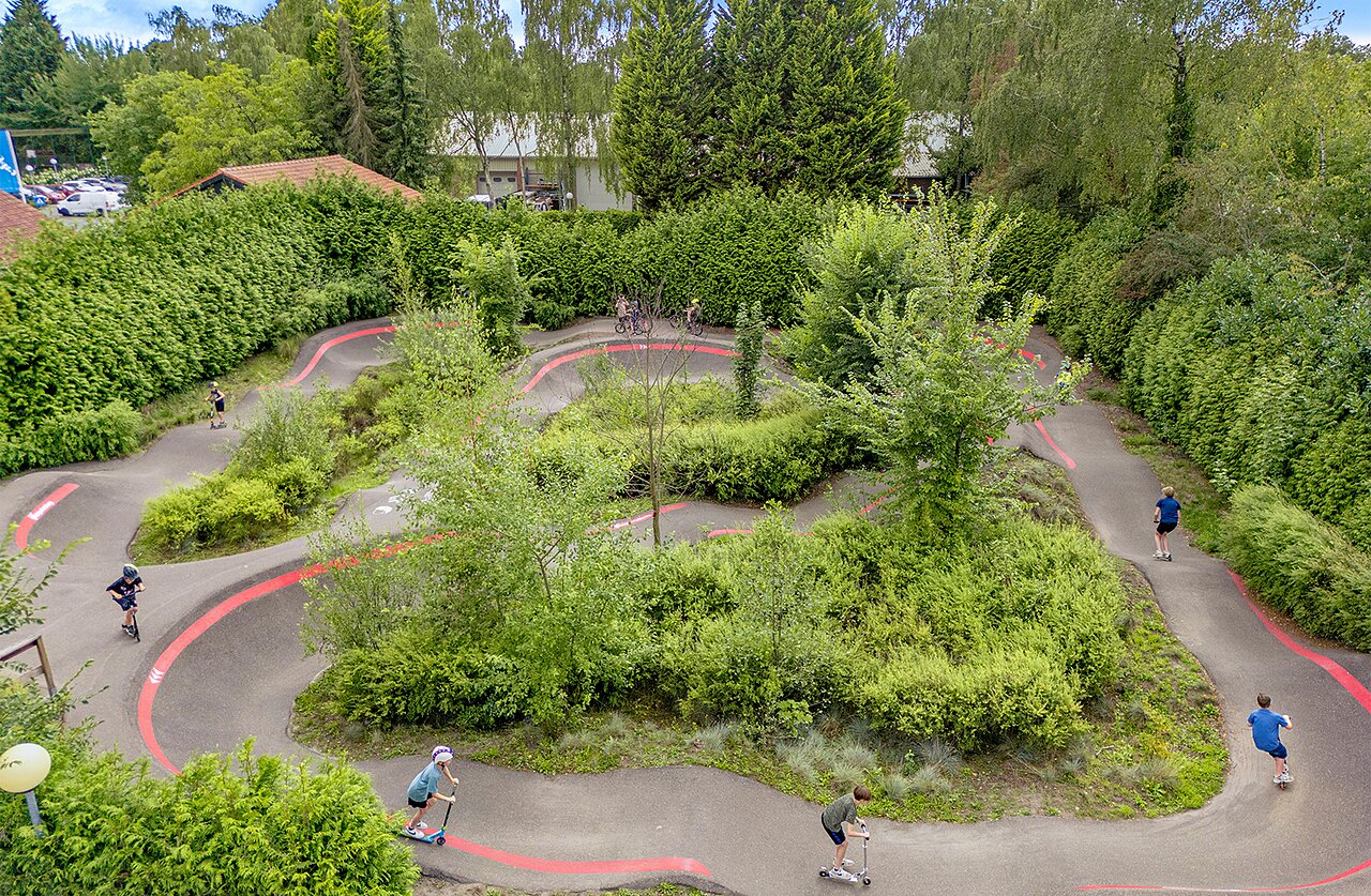 Kinder auf Pumptrack mit Rollern und Fahrr�dern auf Campingplatz CAPFUN Ponderosa in Ulicoten.