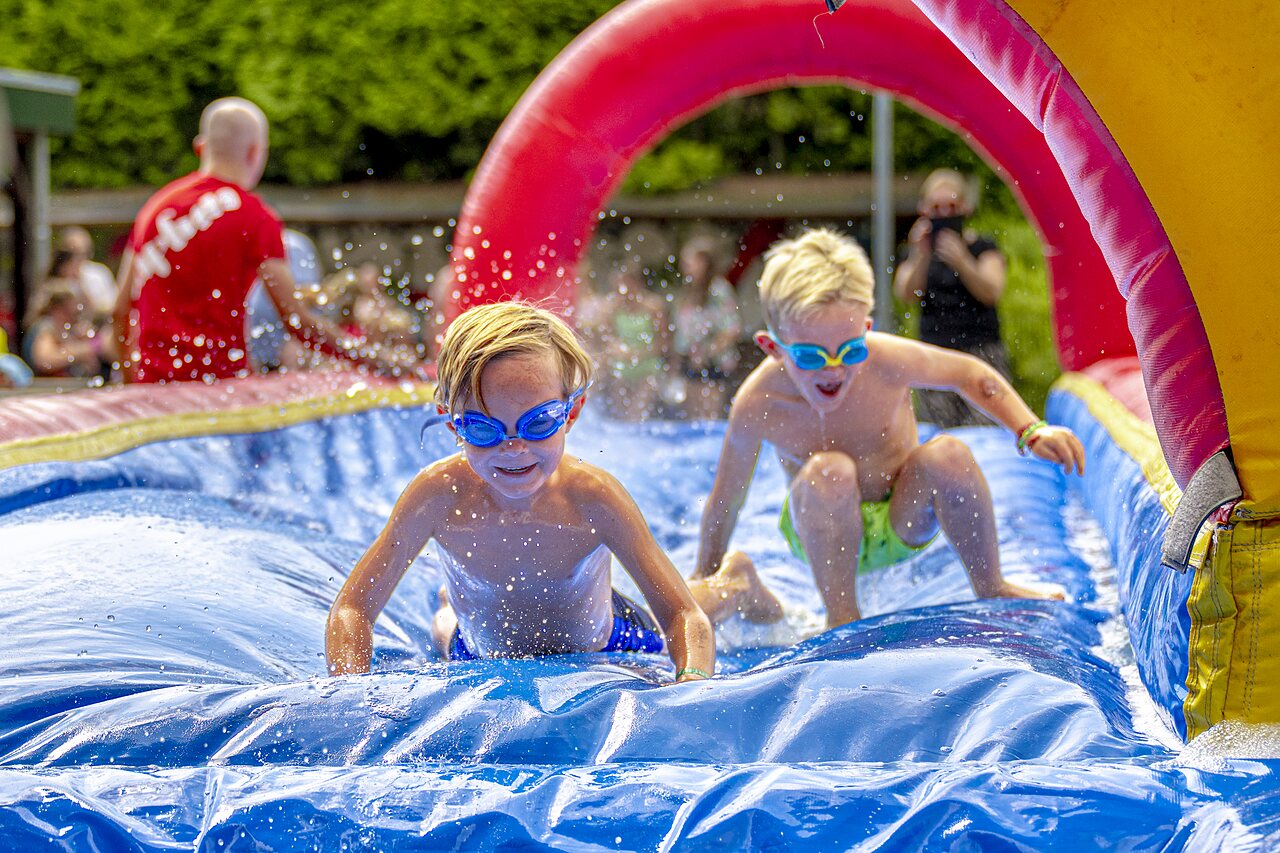 Kinder spielen auf aufblasbarer Wasserrutsche auf dem Campingplatz CAPFUN Ponderosa in Ulicoten.