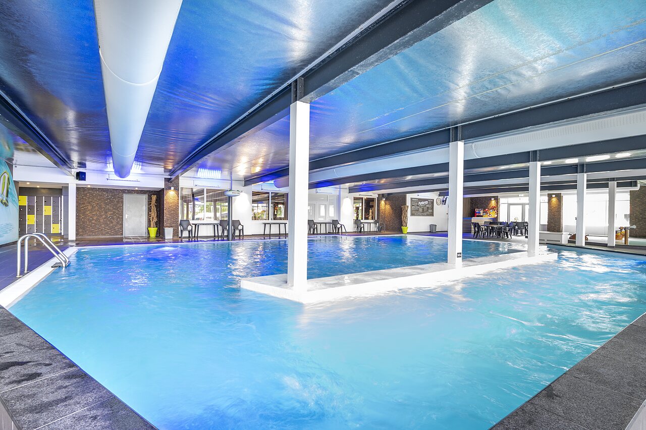 Beheiztes Hallenbad mit blauer Beleuchtung und Entspannungsbereich auf dem Campingplatz CAPFUN Ponderosa in Ulicoten.