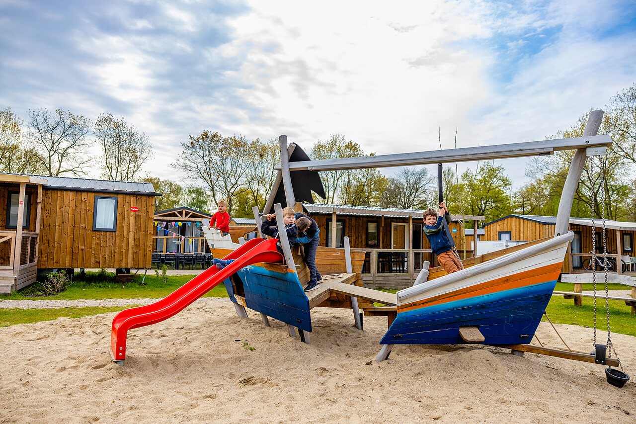 Kinder spielen auf Boots-Spielplatz mit Rutsche auf Camping CAPFUN Ponderosa in Ulicoten.