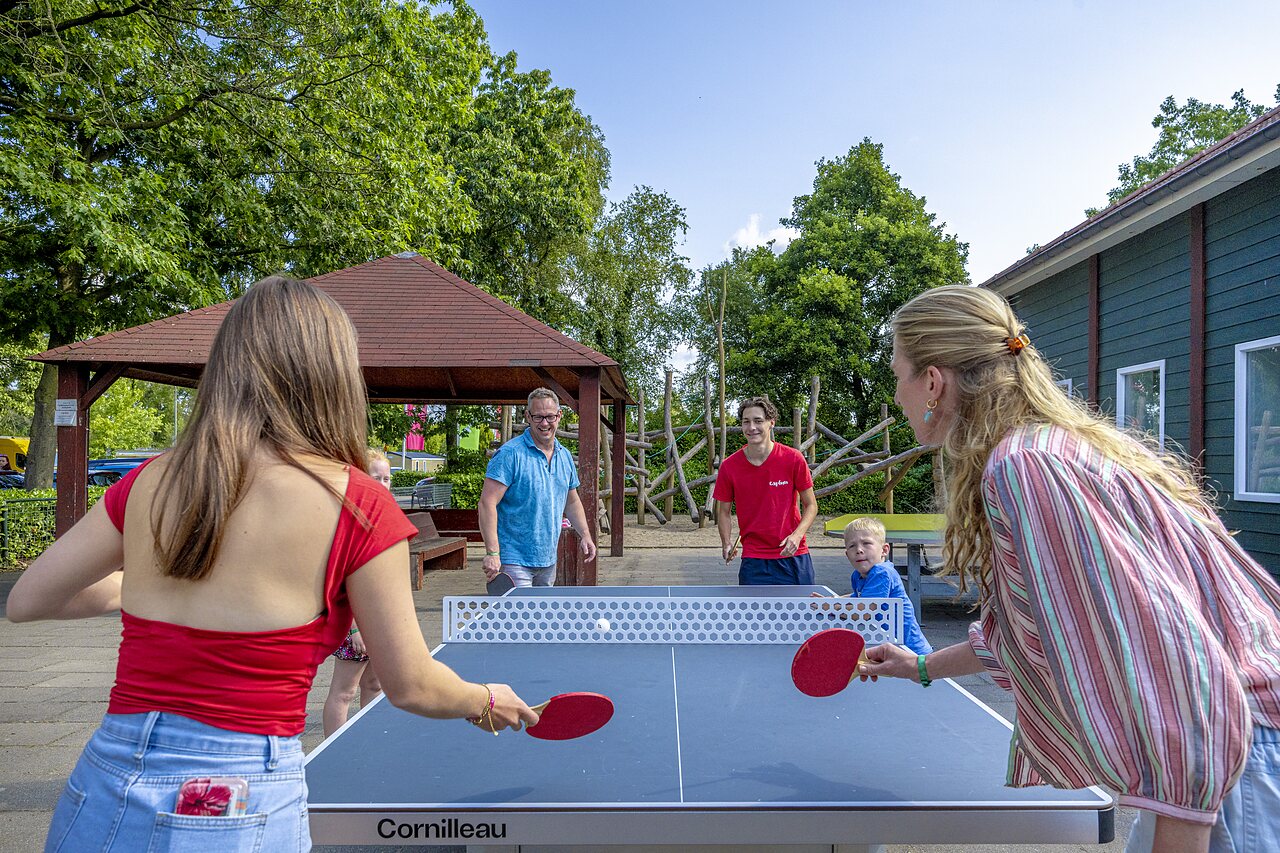 Familie spielt Tischtennis im Freien auf dem Campingplatz CAPFUN Ponderosa in Ulicoten.