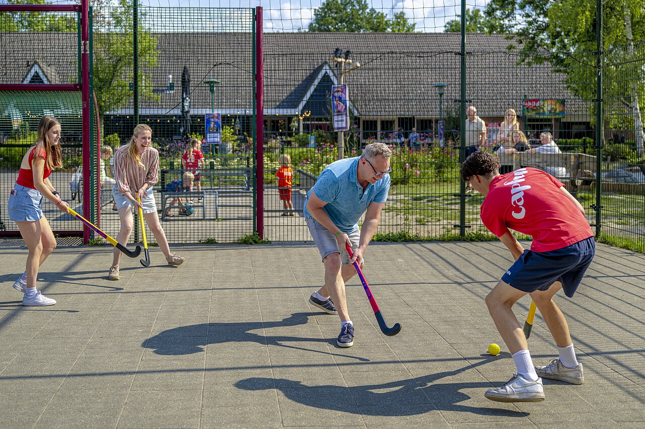 Familie spielt Hockey auf einem Multisportplatz auf dem Campingplatz CAPFUN Ponderosa in Ulicoten.