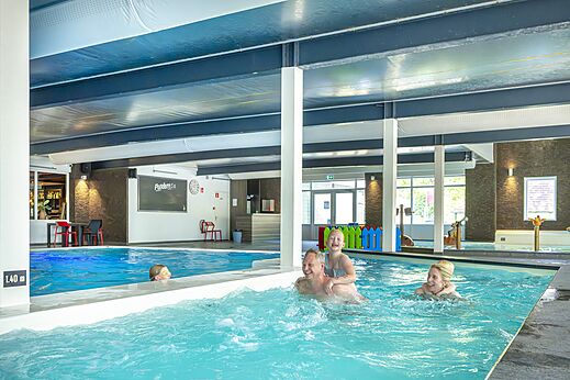 Glückliche Familie schwimmt im beheizten Innenpool auf dem Campingplatz CAPFUN Ponderosa in Ulicoten.