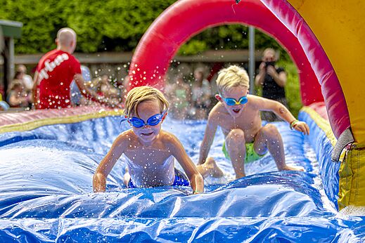 Kinder haben Spaß auf einer aufblasbaren Wasserrutsche auf dem Campingplatz CAPFUN Ponderosa in Ulicoten.