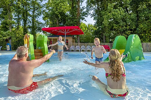 Außenpool mit Wasserspielgeräten und Familie amüsiert sich auf dem Campingplatz CAPFUN Ponderosa in Ulicoten.