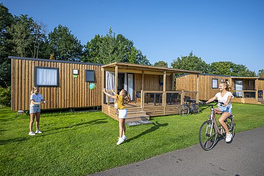 Moderne Holz-Mobilheime mit Terrasse, Kinder spielen auf Camping CAPFUN Ponderosa in Ulicoten.