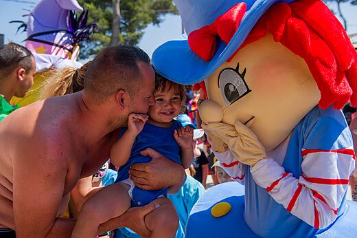 Lächelnder Vater und Kind mit Animationsmaskottchen auf dem Campingplatz CAPFUN Les Portes du Beaujolais in Anse (69).