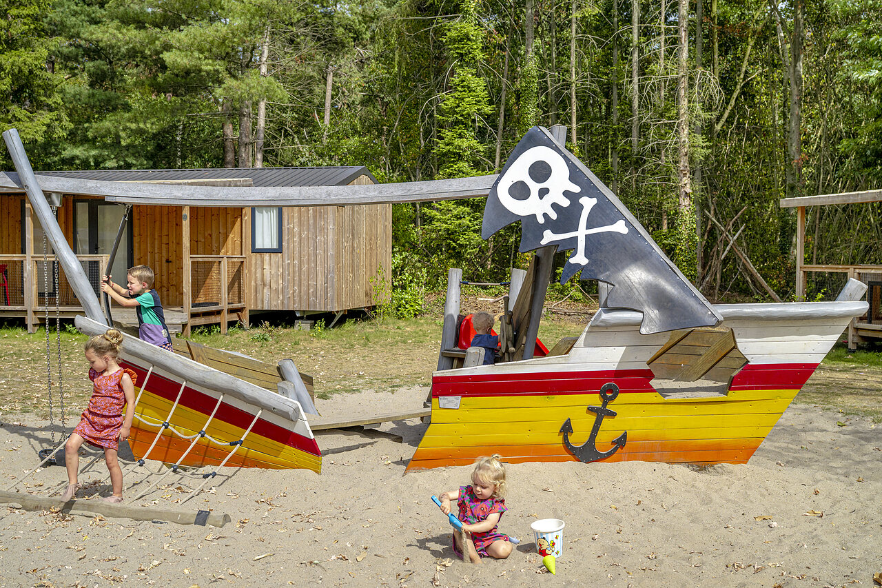 Kinder spielen auf Piratenschiff-Spielplatz mit Mobilheimen auf Camping CAPFUN Rakelbos in Westelbeers.