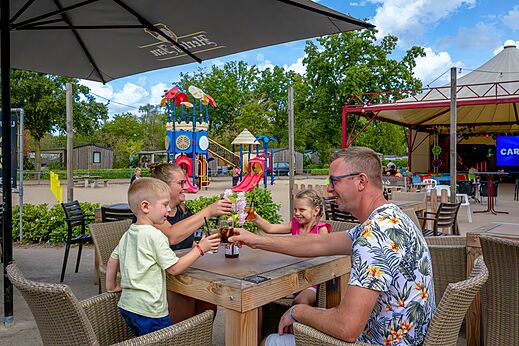 Familie genie�t Bar und Spielplatz auf dem Campingplatz CAPFUN Rakelbos in Westelbeers.