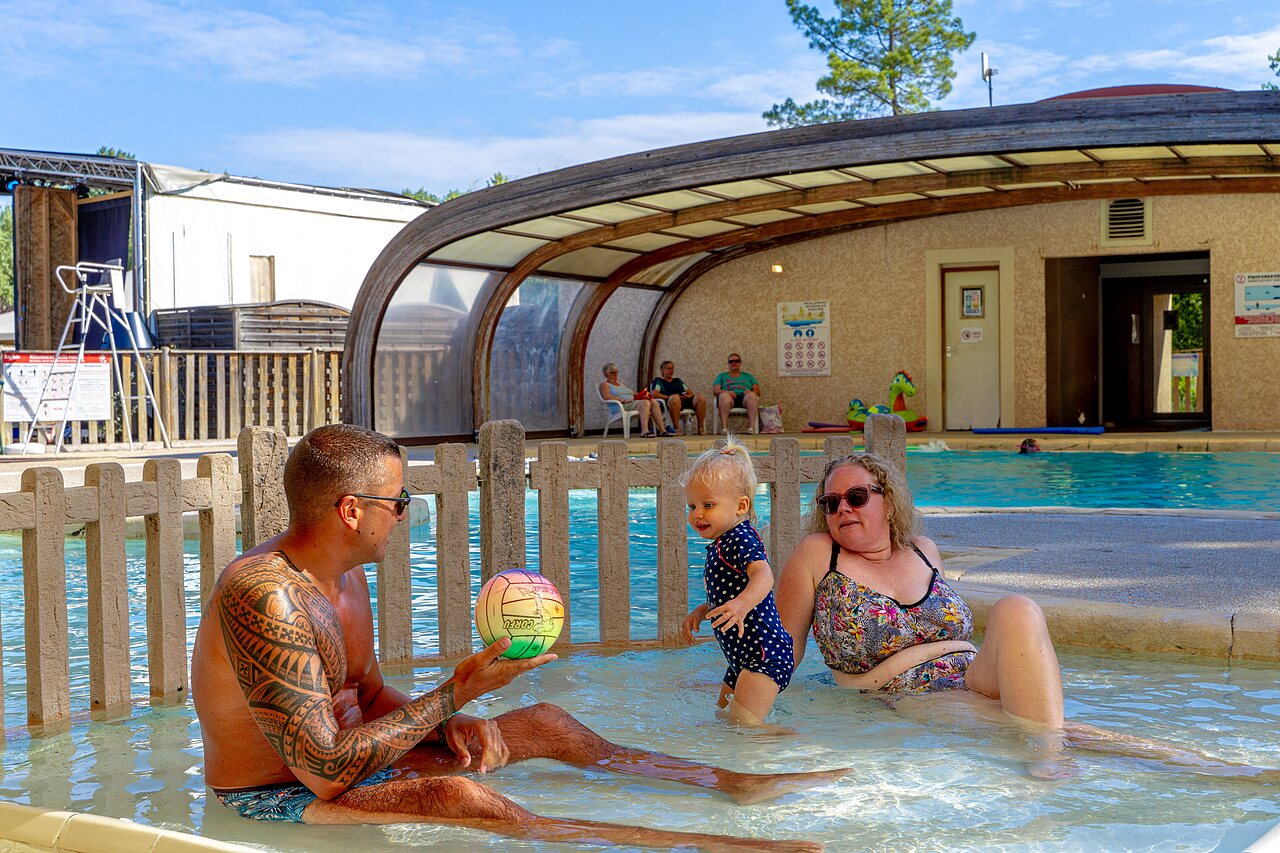 Family with baby in paddling pool, covered swimming pool at CAPFUN R�gni�re campsite in VILLETTE D'ANTHON (38).