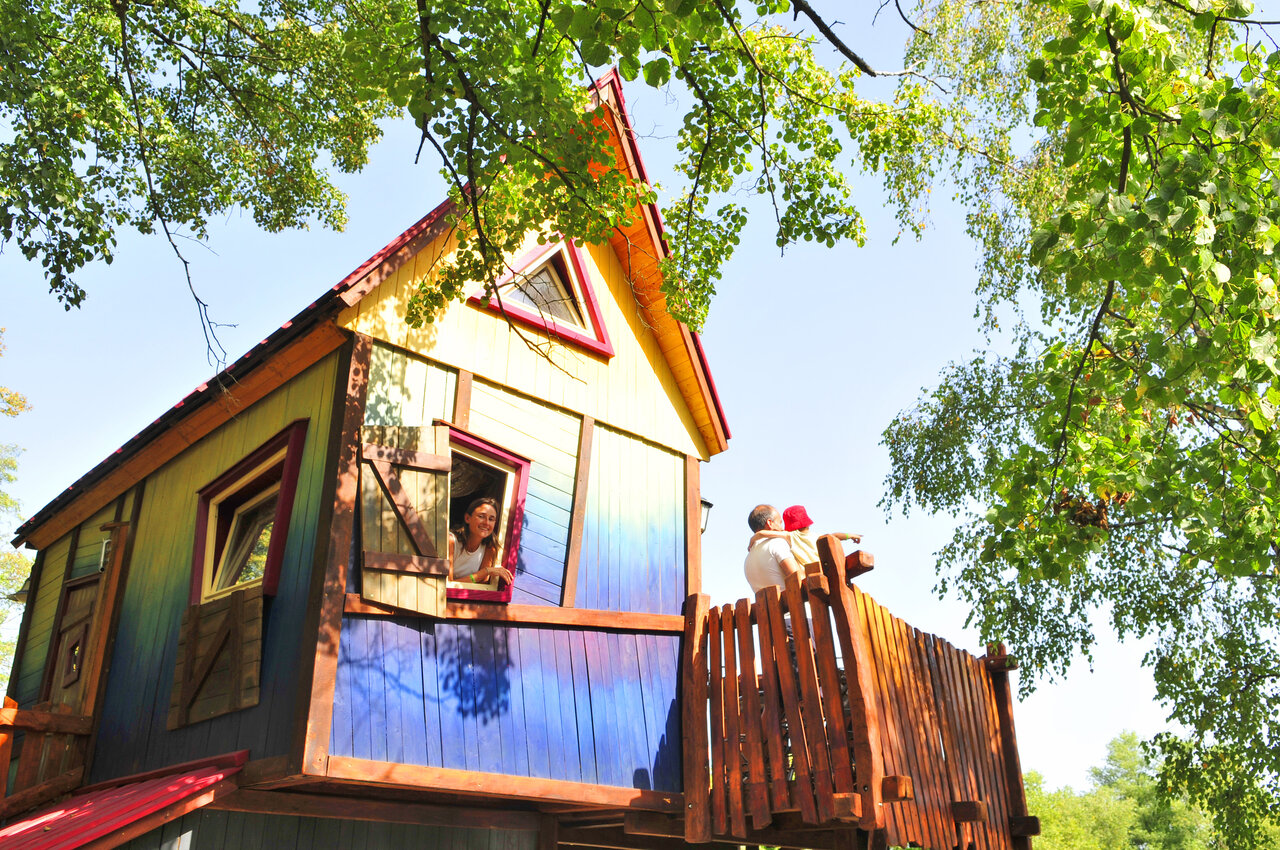 Buntes Baumhaus mit Familie auf Balkon auf dem Campingplatz CAPFUN R�gni�re in Villette d'Anthon.