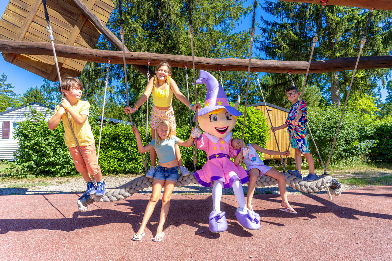 Kinder und Maskottchen auf Riesenschaukel Spielplatz auf Camping CAPFUN R�gni�re in Villette d'Anthon.